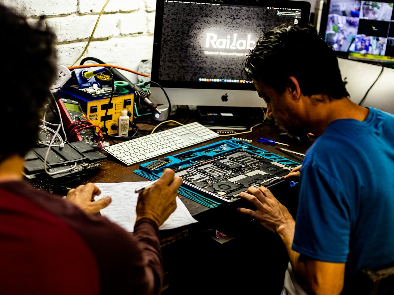Technicians diagnosing and repairing an opened laptop at a service bench